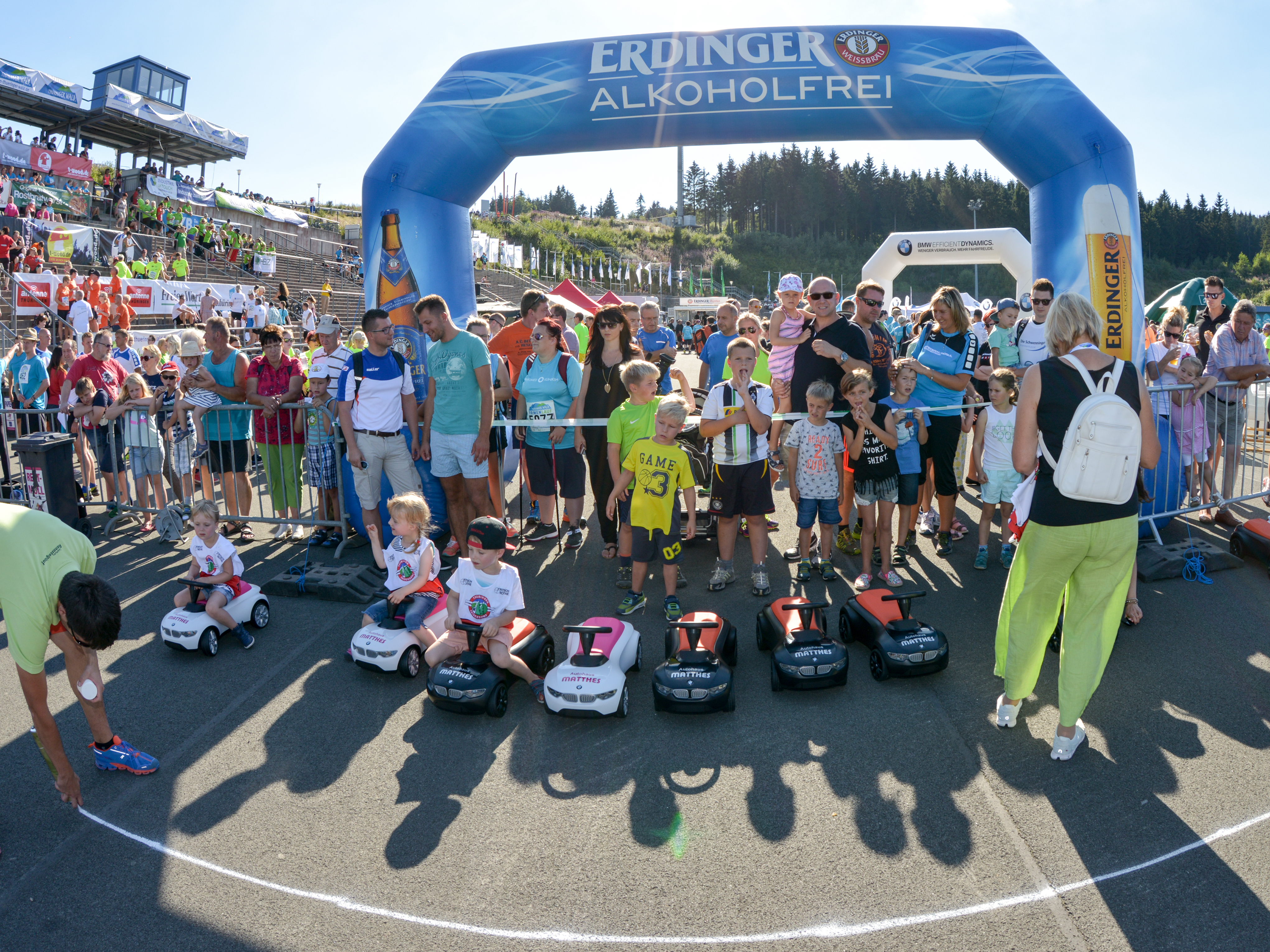 drei der teilnehmenden Kinder am Bobbycar- und Maskottchenrennen beim Thüringer Wald Firmenlauf 2016 sitzen auf den Bobbycars vom Autohaus Matthes und warten auf den Start